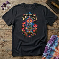 Take Me to Your Shaman lettering above a neon amanita-crowned figure meditating in a glowing forest, on a Black unisex t-shirt