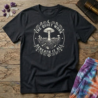 The Quiet Work Beneath It All badge with a mushroom above the soil line and its roots below, on a Black unisex t-shirt