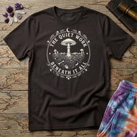 The Quiet Work Beneath It All badge with a mushroom above the soil line and its roots below, on a Dark Chocolate unisex t-shirt