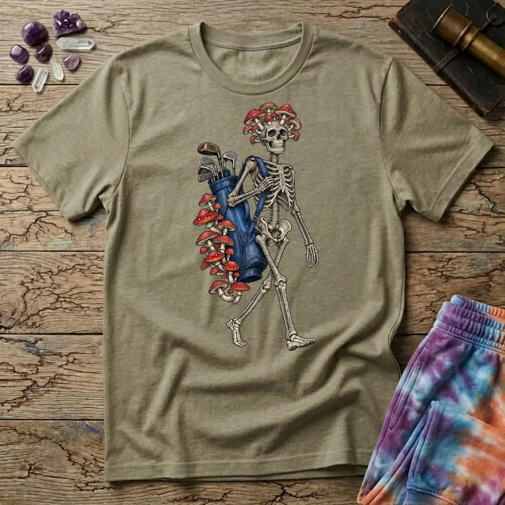 Skeleton carrying a navy golf bag with red amanita mushrooms sprouting from the clubs and skull, on a Sand unisex t-shirt