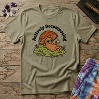 Mushroom in sunglasses kicked back on moss with a coffee, under Actively Decomposing lettering, on a unisex t-shirt
